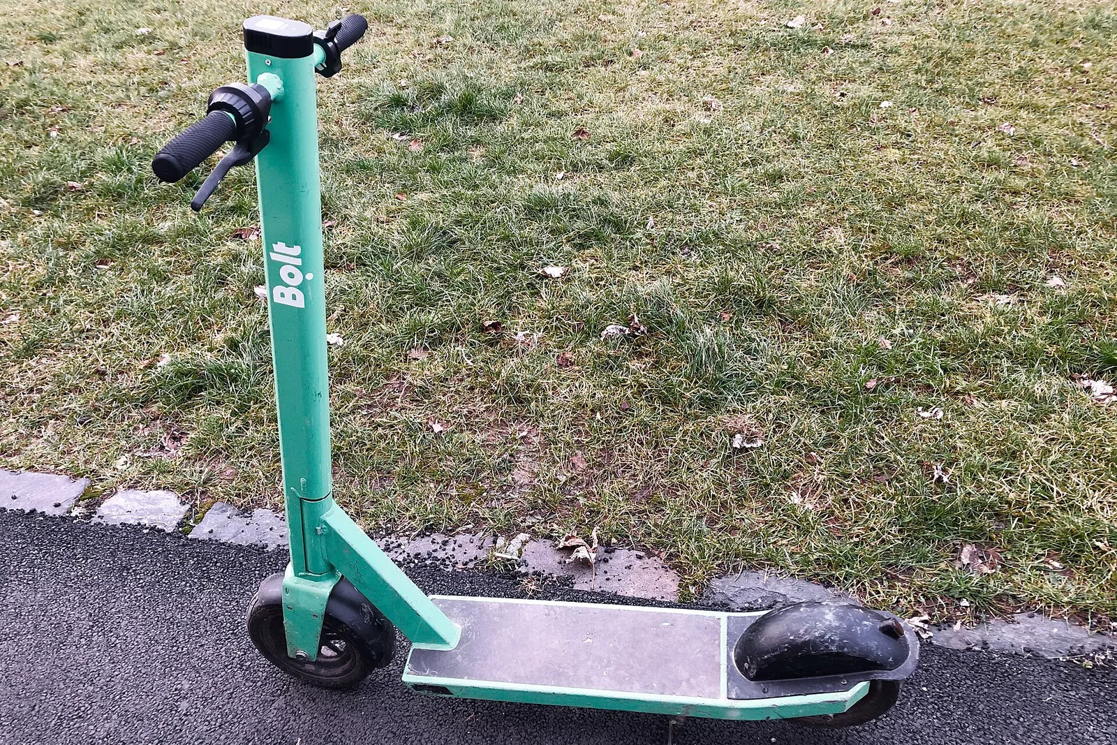 Üksik elektritõukeratas teeäärse muru kõrval.