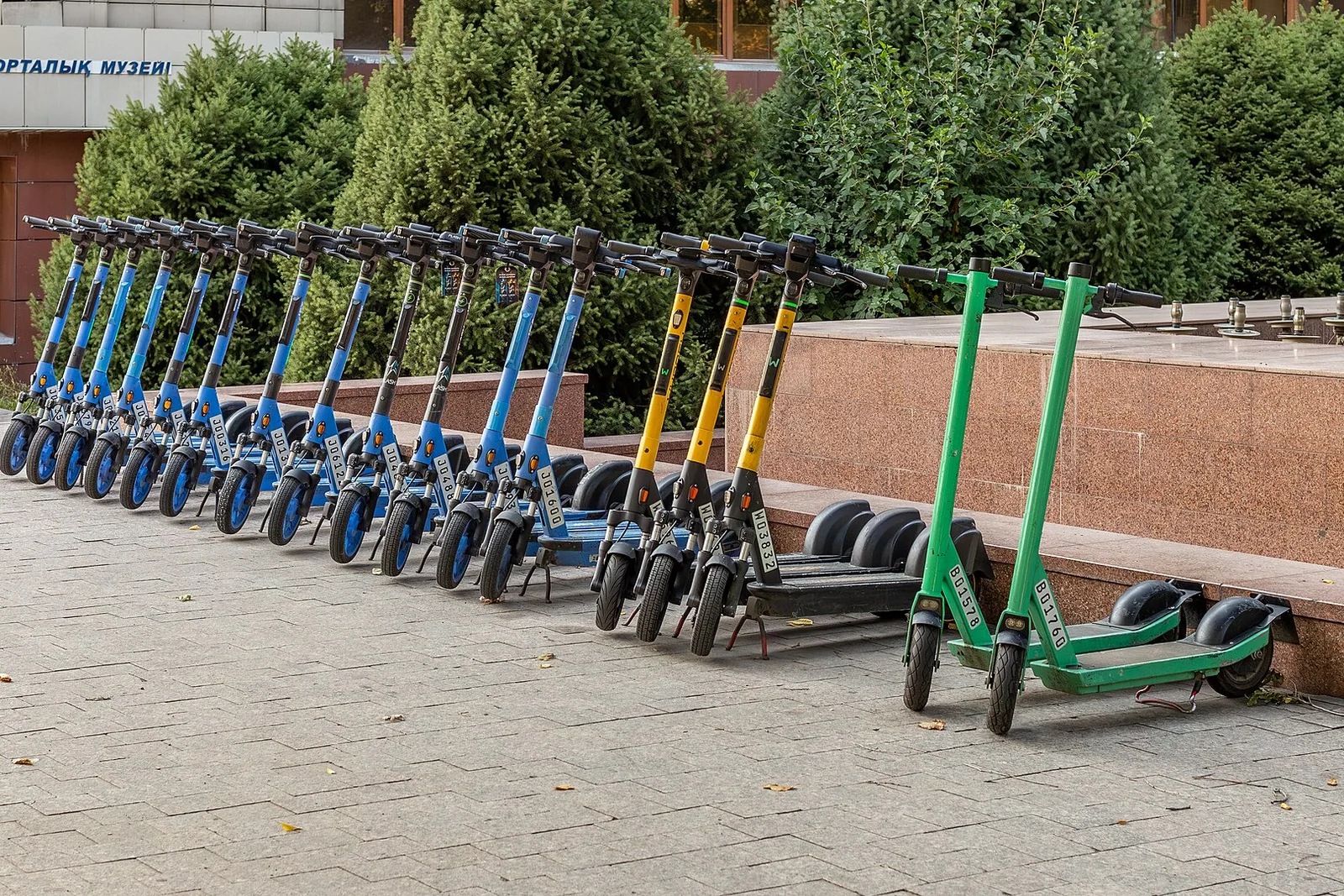 Pikk rida eri värvi elektritõukerattaid linnaväljakul.